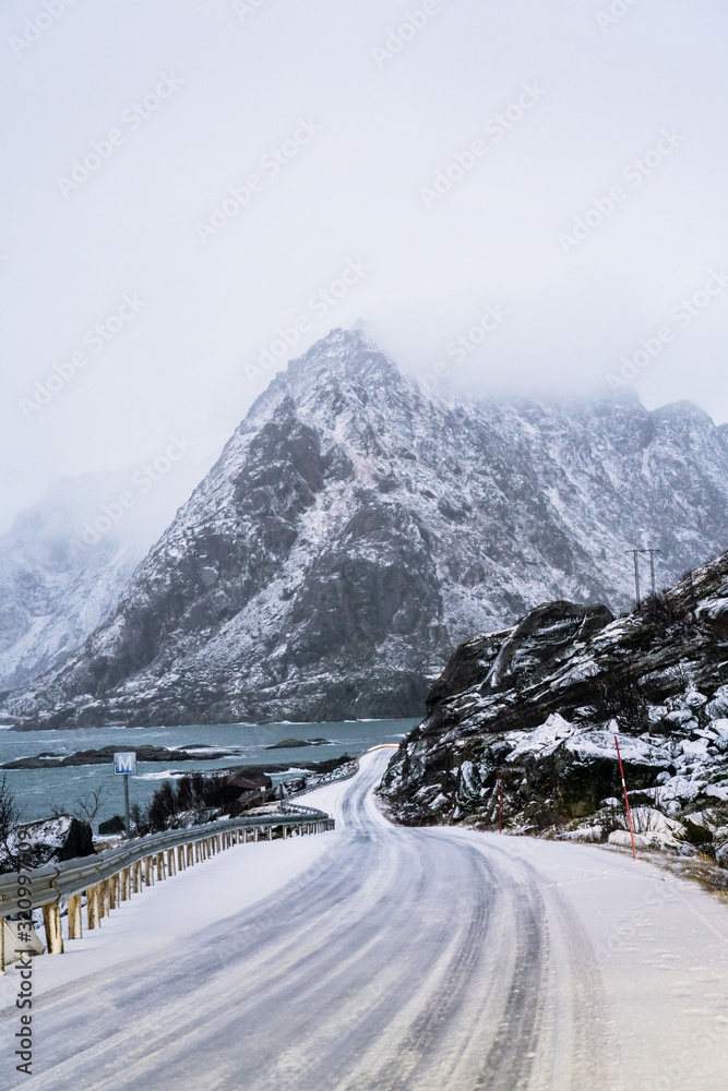 Winter road trip photo with mountains covered with snow and seashore on left side of road.