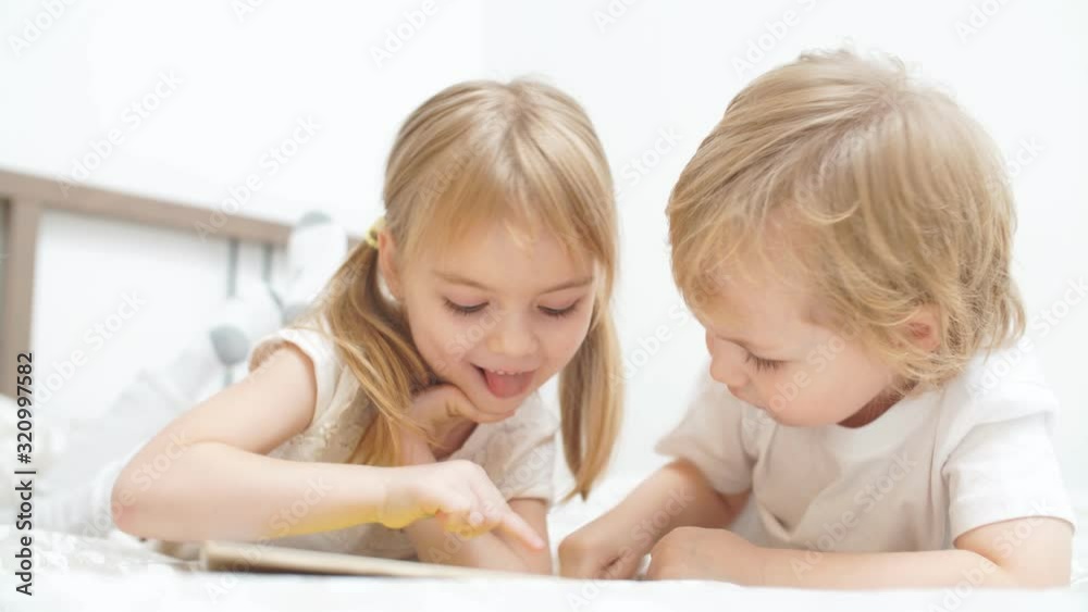 Cute blond kids play games on tablet in a light room. Cute blond kids play games on tablet in a light room.
