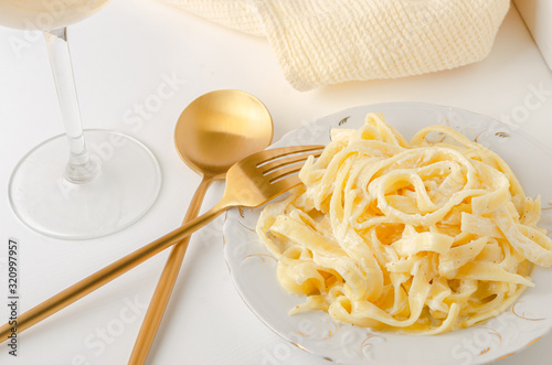 Traditional Italian pasta - Fetuccini Alfredo on a white table with golden appliances