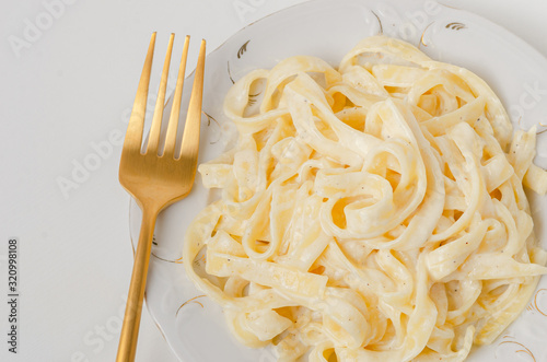 Traditional Italian pasta - Fetuccini Alfredo on a white table with golden appliances photo