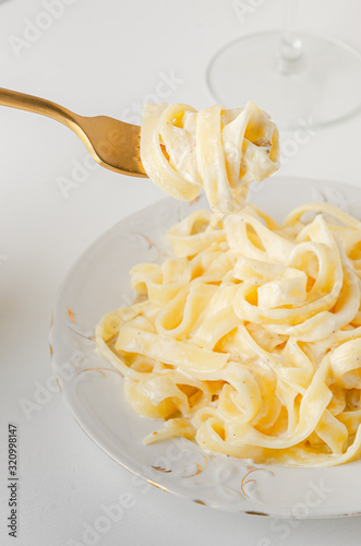 Traditional Italian pasta - Fetuccini Alfredo on a white table with golden appliances photo