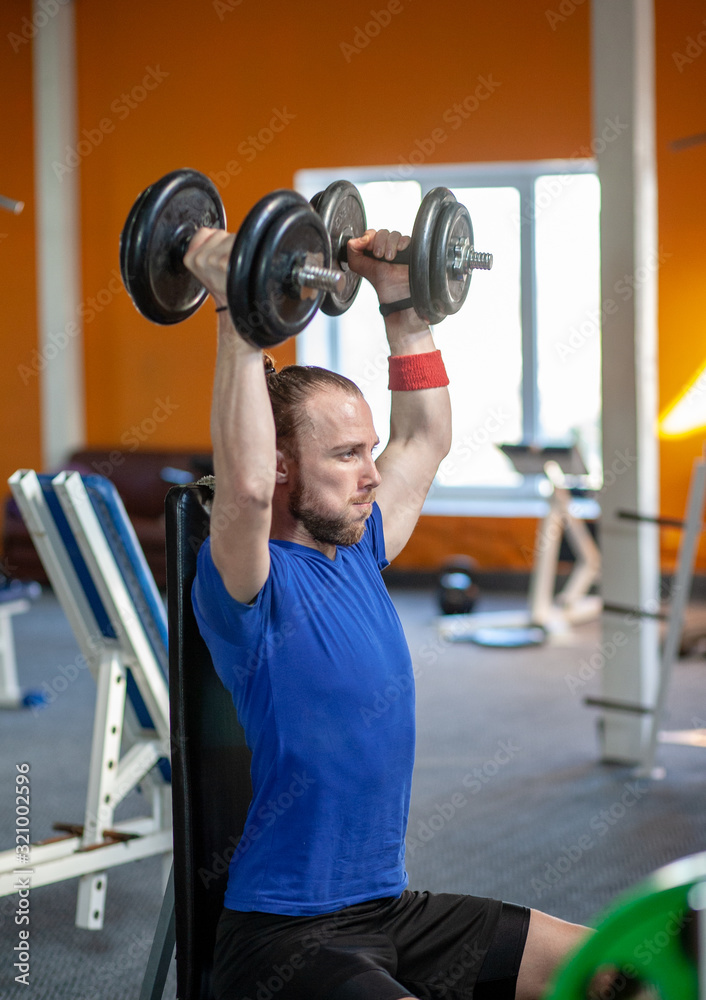 Strong man lifting weight in sport club. Closeup guy training muscles with dumbbells in gym. Handsome fitness trainer doing power lifting exercises in fitness center. Strong man lifting weight in sport club. Closeup guy training muscles with dumbbells in gym. Handsome fitness trainer doing power lifting exercises in fitness center.