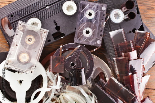 Vintage film camera rolls, old audio and video casettes with tape and foto strip on a wooden background. photo