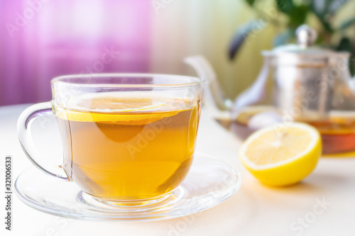 A transparent cup with herbal tea with lemon. In the background is a teapot. The concept of healthy organic drinks.
