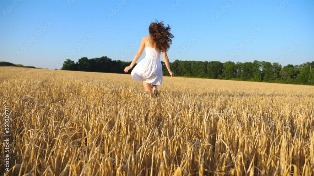 Attractive woman in white dress running through field with yellow ripe wheat. Young carefree girl enjoying freedom in beautiful nature environment. Scenic summer landscape at background. Slow motion Attractive woman in white dress running through field with yellow ripe wheat. Young carefree girl enjoying freedom in beautiful nature environment. Scenic summer landscape at background. Slow motion