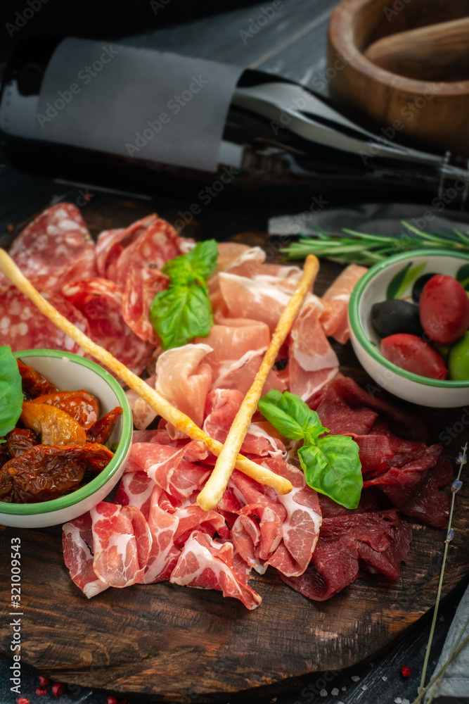 Italian meat appetizers and wine on a wooden tray. Wine snack Antipasto-salami, prosciutto, slices ham, beef jerky and bread sticks.