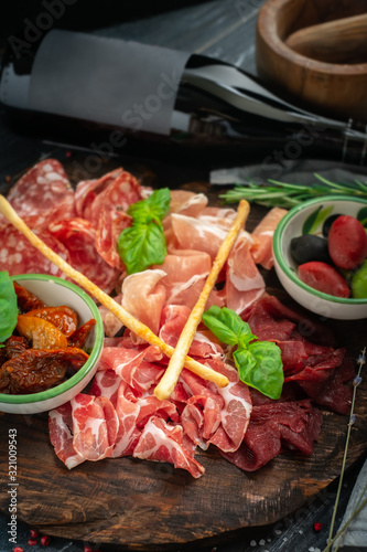 Italian meat appetizers and wine on a wooden tray. Wine snack Antipasto-salami, prosciutto, slices ham, beef jerky and bread sticks.