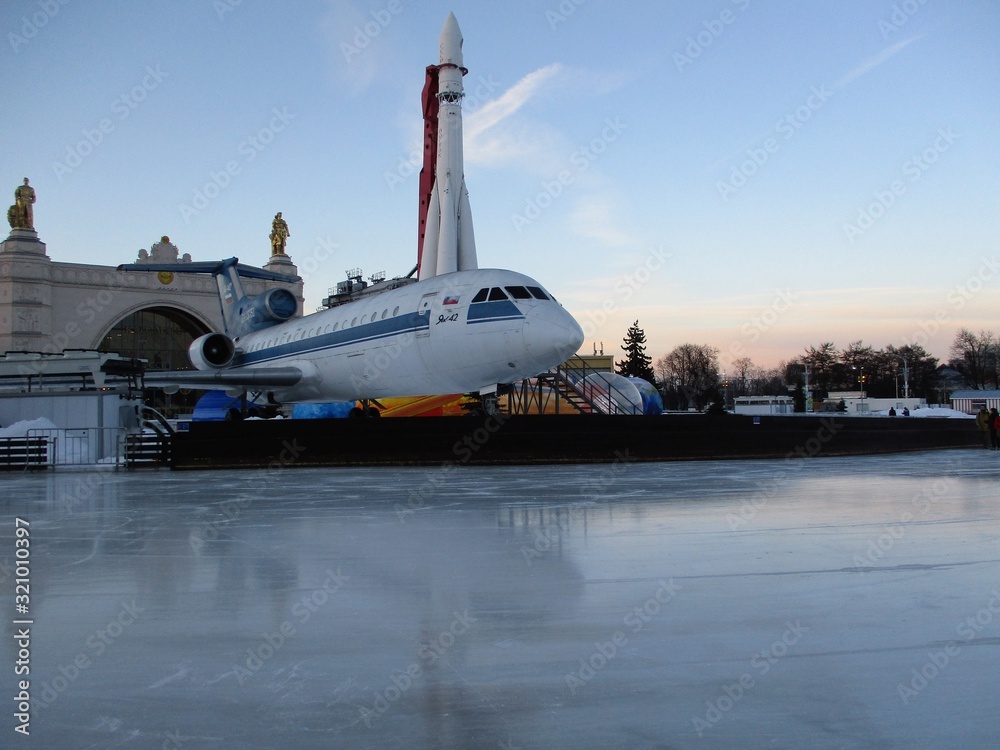 Fototapeta premium Skating rink at Moscow's VDNKh facility with a space rocket and a plane in background