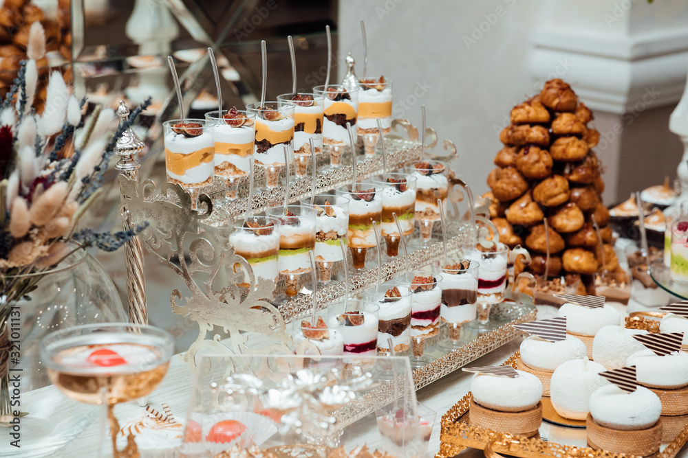 Table full with cakes and sweets at a wedding reception. Wedding candy bar and different cap cakes. Candy bar, a table with sweets and desserts on the table. Buffet with delicious cupcakes, flowers.