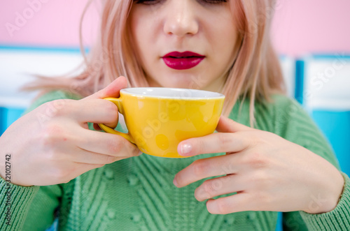 Beautiful young girl with red lipstick drinking tea in cafe. Clouse up photo
