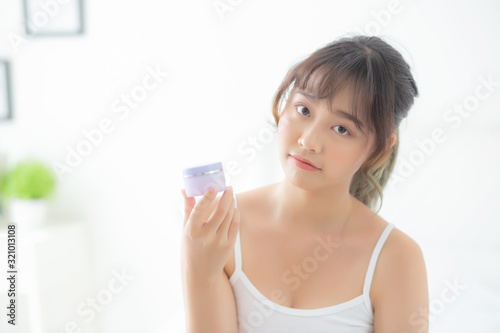 Beautiful portrait young asian woman holding and presenting cream or lotion product, beauty asia girl show cosmetic makeup and moisturizing for skin care, healthy care and wellness concept.