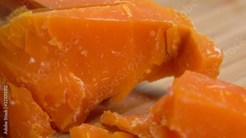 Knife cuts and breaks a hard french orange-colored Mimolette cheese on a wooden board photo