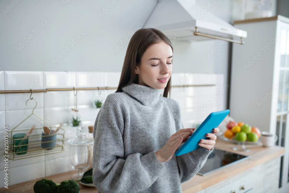 Dark-haired girl in a grey sweater reading something on her tablet Dark-haired girl in a grey sweater reading something on her tablet
