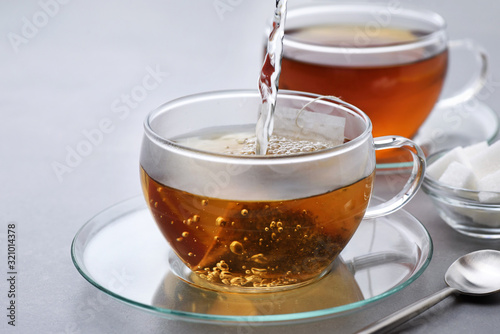 Hot water pours into a cup with a tea bag on a gray background. photo