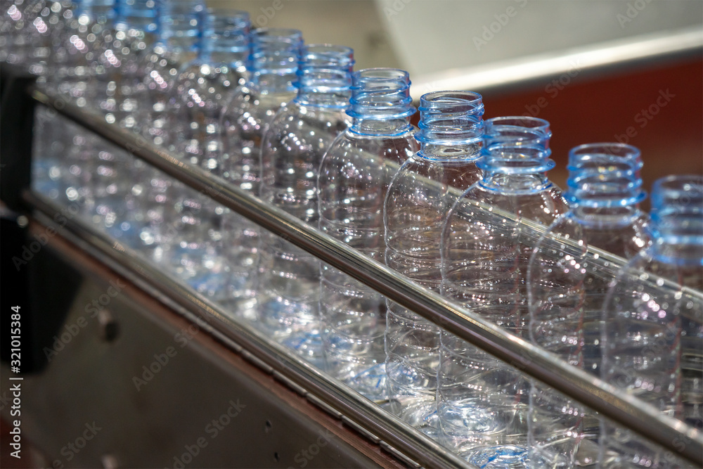 The PET bottles in the rail on the conveyor belt for filling process in the drinking water factory. The drinking water factory production process by automatic filling machine in the plant. The PET bottles in the rail on the conveyor belt for filling process in the drinking water factory. The drinking water factory production process by automatic filling machine in the plant.