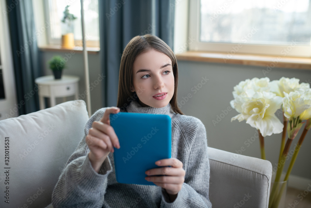 Dark-haired girl in a grey sweater with a tablet looking thoughtful Dark-haired girl in a grey sweater with a tablet looking thoughtful