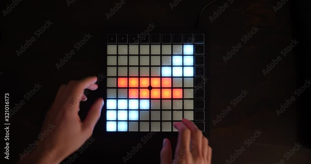 An electronic music producer using a digital midi instrument in a studio with led lights.