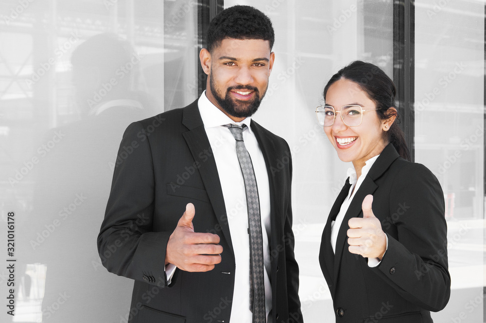 Happy confident business partners enjoying teamwork. Smiling young man and woman in office suits showing thumb up gestures. Best team concept Happy confident business partners enjoying teamwork. Smiling young man and woman in office suits showing thumb up gestures. Best team concept