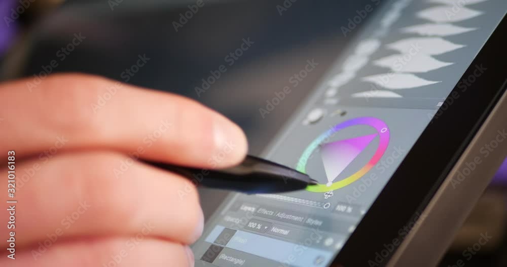 A freelance digital artist or designer selecting a color hue and painting with a drawing graphic tablet and pen in an art studio.