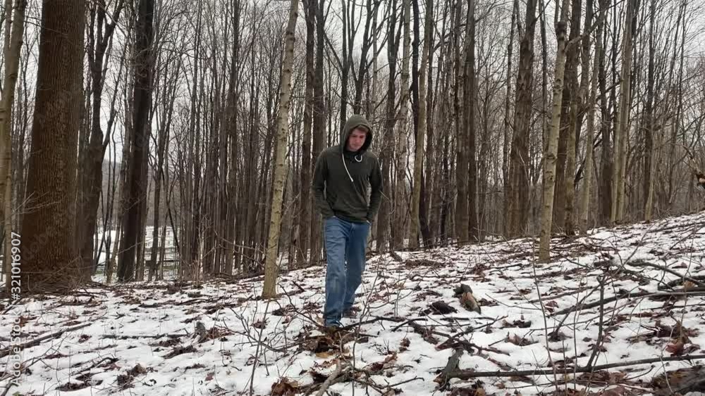 Young man walking slowly through the woods on a hike in winter time. Young man walking slowly through the woods on a hike in winter time.