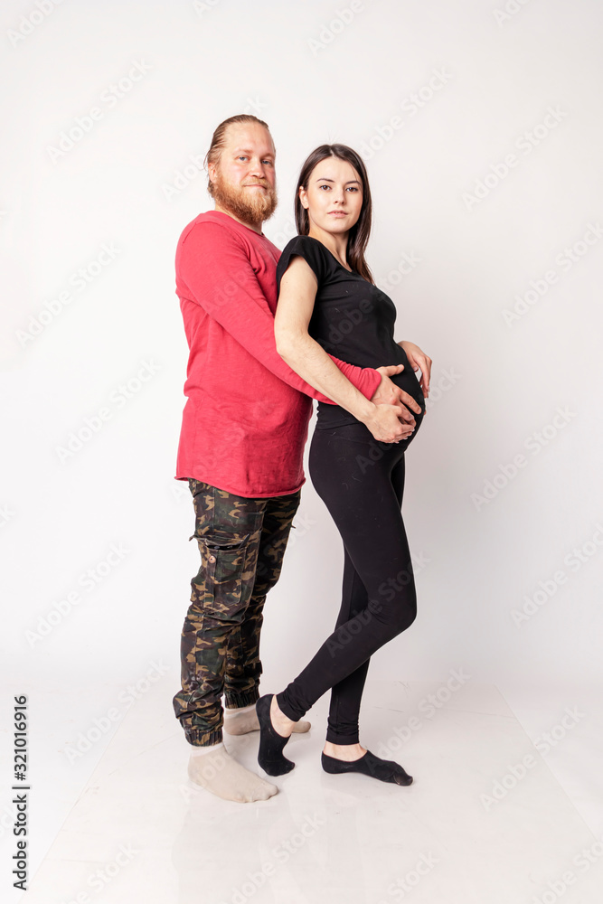 Fototapeta premium Caucasian man with a beard in a red sweater hugs a pregnant Caucasian girl