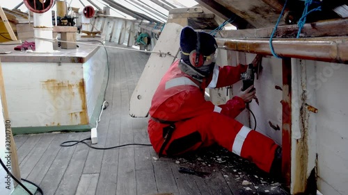 Young woman seaman sanding the planks on a traditional wooden schooner in Grimstad, Norway