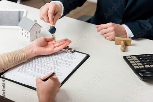 cropped view of realtor giving key to woman signing agreement, leasing concept