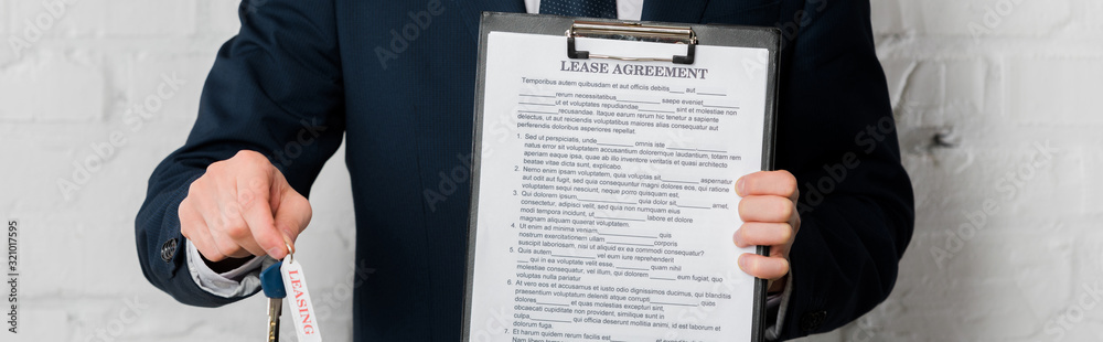 panoramic shot of realtor holding key and clipboard with lease agreement on white