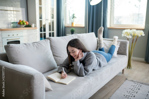 Young girl in a grey sweater laying on the sofa