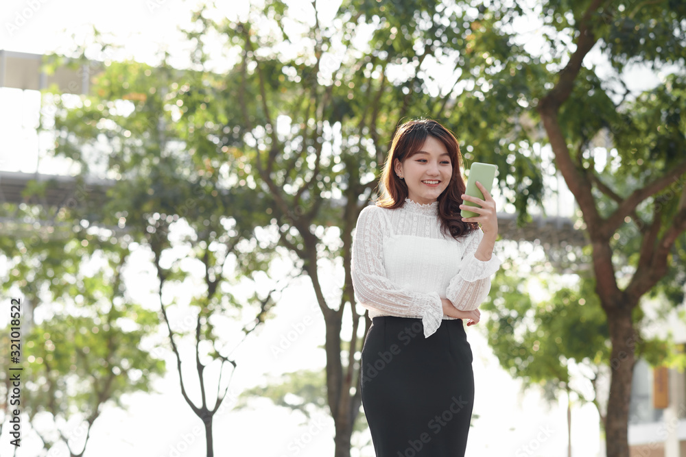 Lifestyle portrait of happy woman walking in the city on a sunny summer day typing text message on smartphone device Lifestyle portrait of happy woman walking in the city on a sunny summer day typing text message on smartphone device