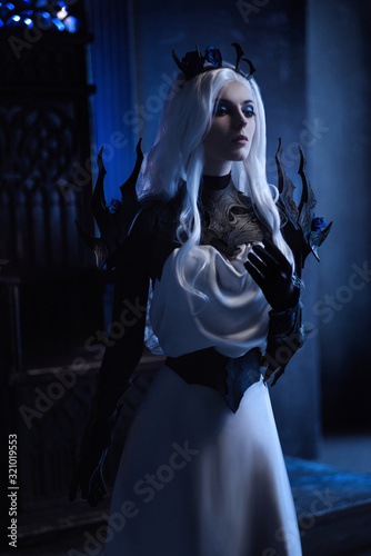 Attractive blonde woman in fantasy costume of dark queen sitting on throne in castle