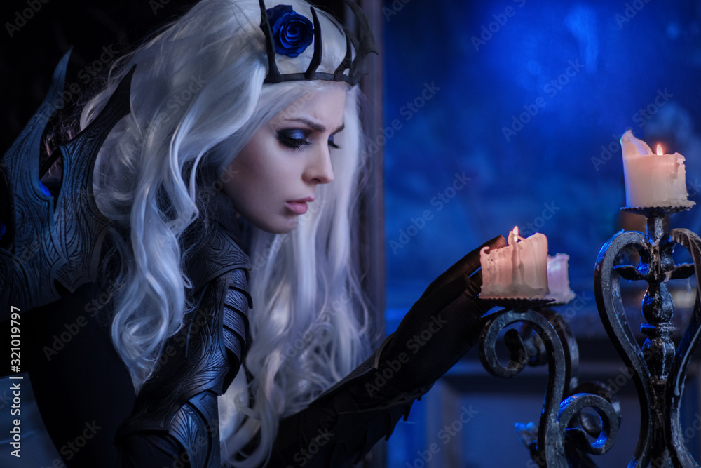 Foto Stock Attractive blonde woman in fantasy costume of dark queen firing  candle | Adobe Stock