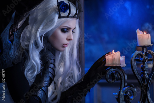 Attractive blonde woman in fantasy costume of dark queen firing candle 