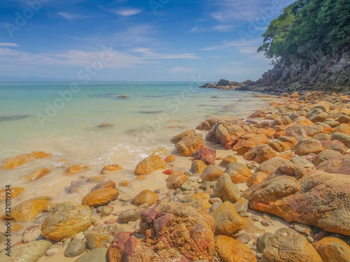 view of many rocks on sand beach with blue-green sea and blue sky background, Kwang Peeb Beach (Ao Kwang Peeb), Ko Phayam island, Ranong, Thailand.