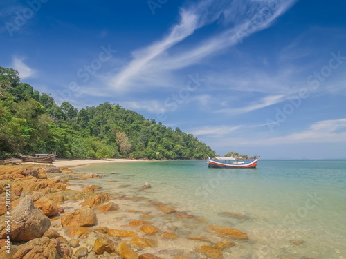 view of many rocks on sand beach with a fishing boat floating in blue-green sea and blue sky background, Kwang Peeb beach (Ao Kwang Peeb), Ko Phayam (ko payam), Ranong, Thailand.