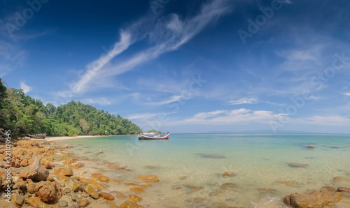 view of many rocks on sand beach with a fishing boat floating in blue-green sea and blue sky background, Kwang Peeb beach (Ao Kwang Peeb), Ko Phayam (ko payam), Ranong, Thailand. photo