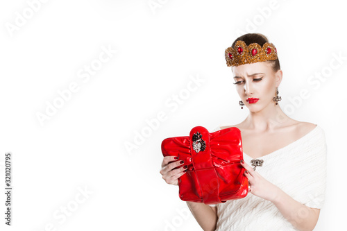 Portrait of young unhappy poor crowned beauty queen frustrated woman holding looking in her bag wallet happy looking into it, not having money photo