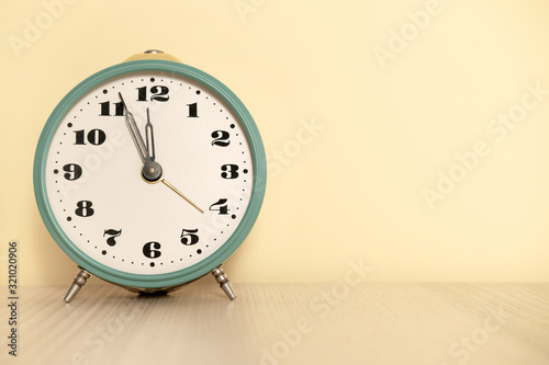 Antique analog clock with hands set at 12:00. 11:55 a.m. 00:00 12:00 24:00. The alarm clock is on the table photo