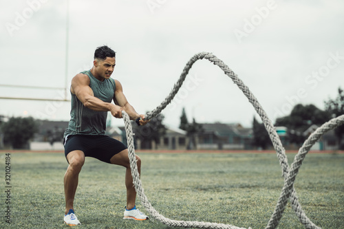 Fotografie Man doing workout using battle ropes on the ground