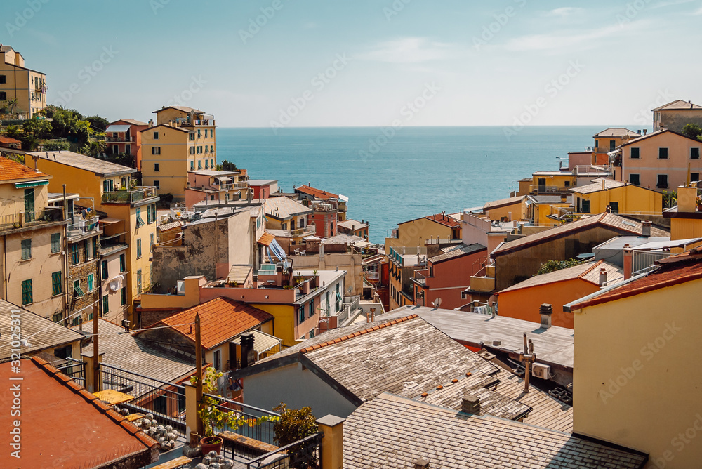 Top view of tiled roofs of colorful houses with balconies and green shutter windows of Riomaggiore, a typical fishing village in the Cinque Terre National Park, the blue Ligurian Sea is on the horizon