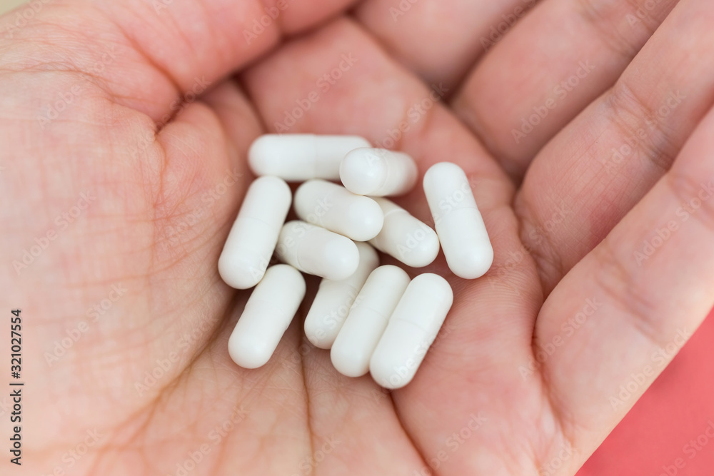 A handful of white medical capsules of medicine in the palm of hand. Medical background A handful of white medical capsules of medicine in the palm of hand. Medical background