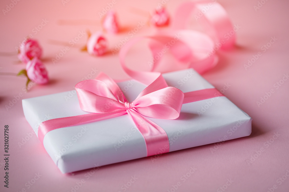 Gift box wrapped in white paper with pink ribbon