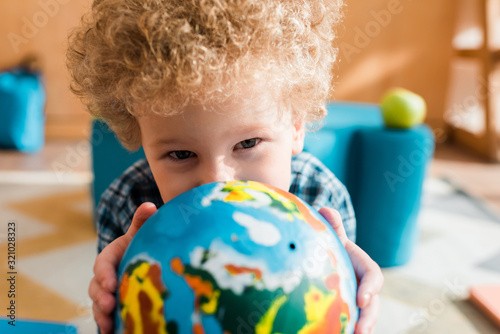 selective focus of smart kid holding globe and looking at camera