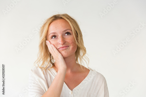Pensive young woman with hand on cheek. Portrait of thoughtful young woman holding hand on face and looking up. Dream concept