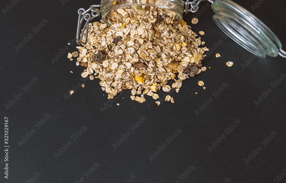 granola spilled out of a glass jar on a black background