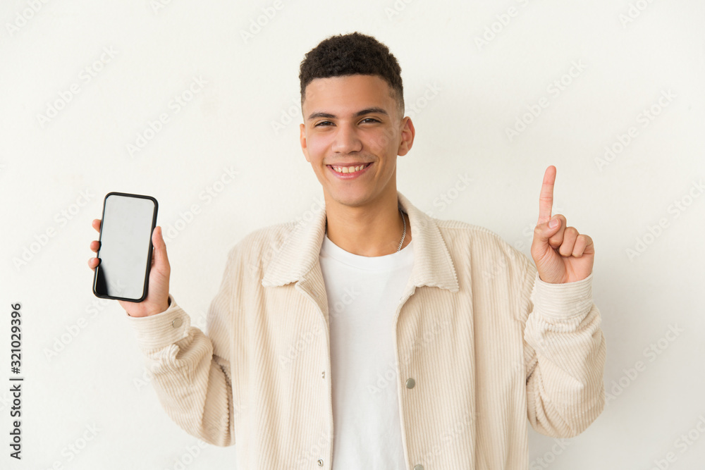 Happy young man showing smartphone. Handsome cheerful young man holding cell phone with blank screen and pointing up with finger. Technology and promotion concept Happy young man showing smartphone. Handsome cheerful young man holding cell phone with blank screen and pointing up with finger. Technology and promotion concept