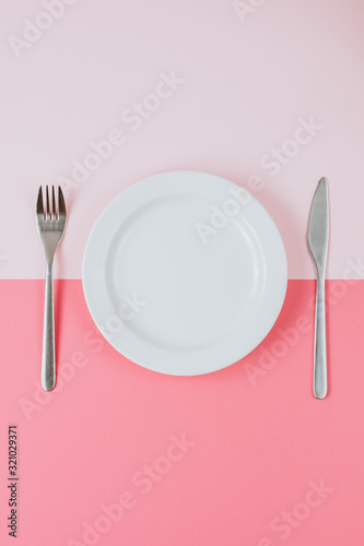 Empty white plate with cutlery on a pink-peach background. Top view. Vertical