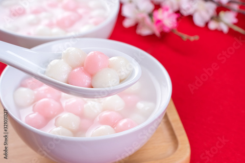 Tang yuan, tangyuan, delicious red and white rice dumpling balls in a small bowl on red background. Asian festive food for Chinese Winter Solstice Festival, close up.