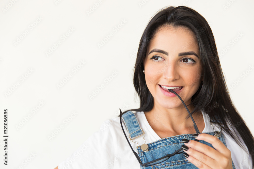 Smiling woman biting spectacles and looking aside. Portrait of beautiful happy young woman holding eyeglasses and looking away isolated on white background. Emotion concept Smiling woman biting spectacles and looking aside. Portrait of beautiful happy young woman holding eyeglasses and looking away isolated on white background. Emotion concept