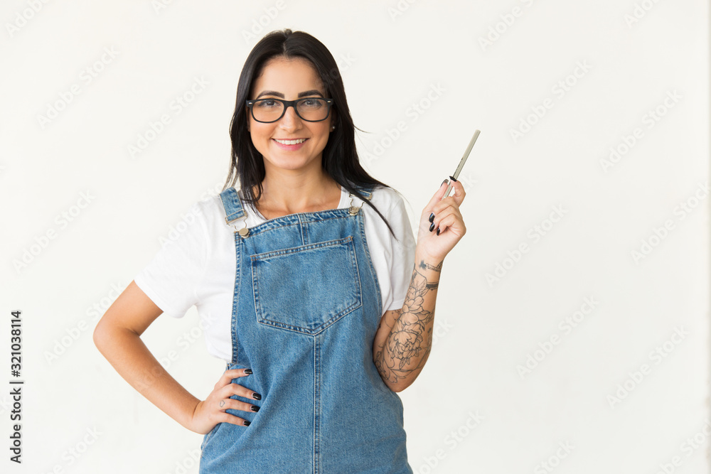 Content woman holding pen and smiling at camera. Cheerful young female student in eyeglasses standing with hand on waist and looking at camera. Education concept Content woman holding pen and smiling at camera. Cheerful young female student in eyeglasses standing with hand on waist and looking at camera. Education concept